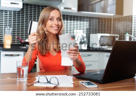 Happy Woman holding bills shopping online with credit card and computer at he kitchen. Internet Shopping. Home banking.