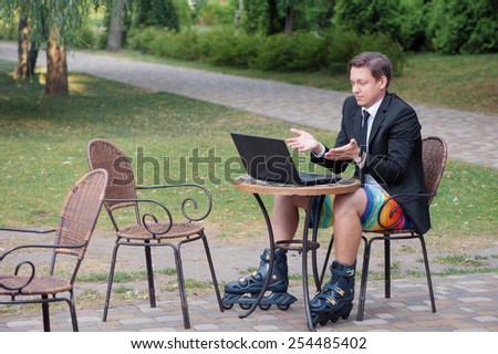 Work and relax. Businessman dressed in suit, shorts and rollers working with laptop at the outdoors cafe