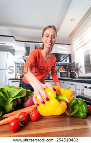 Wide angle view of young woman making healthy food standing happy smiling in kitchen holding pepper. Focus on pepper.