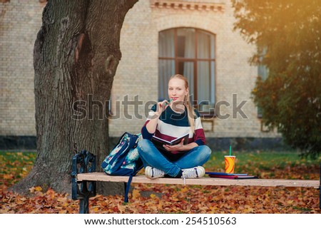 Studying outdoors. Confident attractive young female student studying while sitting in autumn park