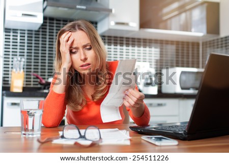 stressed young woman is doing banking and administrative work holding bills at home