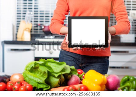 digital recipes book. Cheerful young woman holding digital tablet standing in her kitchen at home