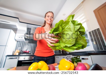 Wide angle view of young caucasian woman making healthy food standing happy smiling in kitchen holding salad. Focus on salad