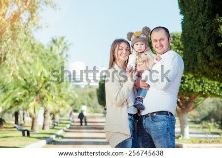 outdoors portrait of happy family wearing casual. Mom and dad holding little kid with funny hat.