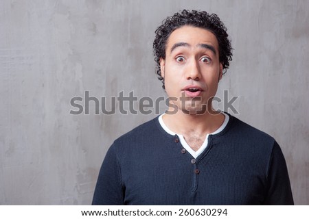 Wow! Surprised young Arabic man in casual wear staring at camera while standing against grey background