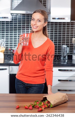 Portrait of a young woman holding glass of water in the kitchen at home