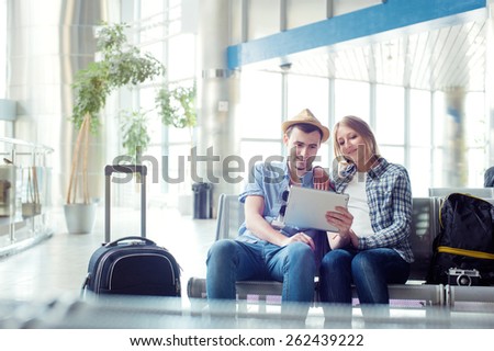 Digital technology and traveling. Young loving couple in casual wear using tablet computer while sitting in the airport terminal waiting for boarding.