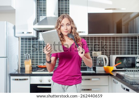 digital recipes book. Thoughtful young woman using digital tablet standing in her kitchen at home