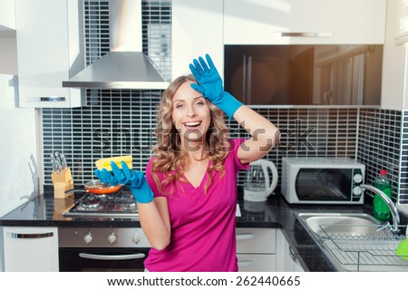 Tired but happy. Cheerful young woman with blue rubber gloves cleaning her kitchen.