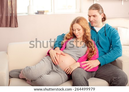 Family couple. Husband and 7 months pregnant wife sitting on the sofa at home.
