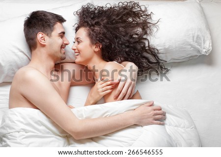 Good morning! Love and comfort. Overhead of happy beautiful young couple lying on the bed laughing and hugging. Top view.