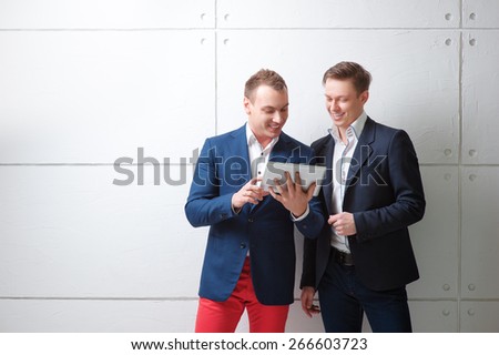 Creative work and technology. Two smiling handsome men using tablet computer while discussing something against white wall.