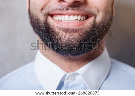Perfect beard. Close-up of young bearded smiling man standing against grey background
