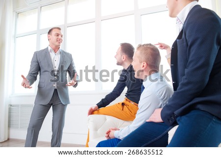 Leadership and charisma. Business speech. Handsome young man in grey suit talking to his colleagues - group of young people.
