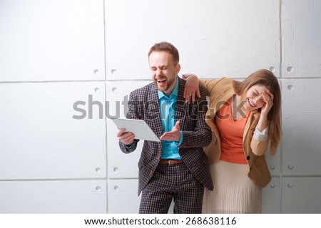 LOL! Watching funny video or reading a joke. Creative work and technology. Young man and woman using tablet computer and laughing against white wall.