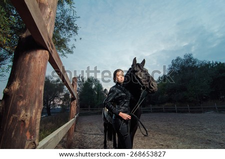 Elegant young woman walking with black horse against moody sky.