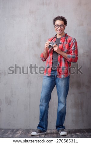 Cheerful photographer. Handsome young Arabic man holding old-fashioned camera and looking at camera while standing against grey background