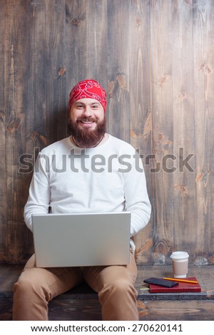 Workplace. Young bearded man using laptop while sitting over wooden background.