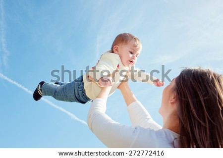 Mother throws up her baby in the sky in nature. View through the mom\'s shoulder.