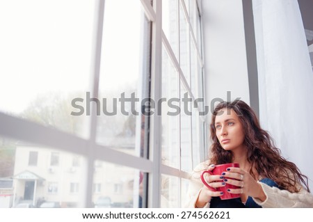 Calm and coziness. Beautiful young woman with cup of tea sitting near the window at home.