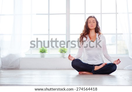 Yoga at home. Keep calm. Attractive young woman sitting on lotus position on floor with eyes closed.