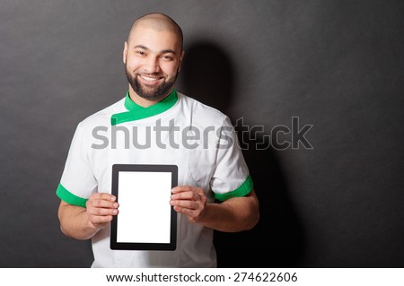 Digital menu. Handsome young arabic chief cook holding tablet computer against blackboard.