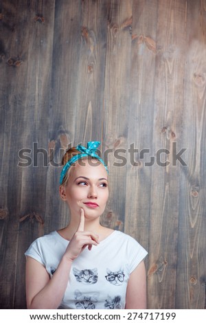 Thinking about solution. Young blond thoughtful woman holding finger on chin against wooden wall.