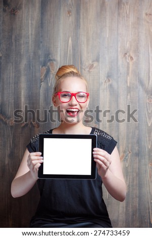 Copy space on screen. Young attractive blond woman holding tablet computer and looking at camera against wooden wall.