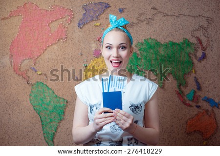 Travel around the world. Young happy woman holding passport and tickets while standing against wall with world map.
