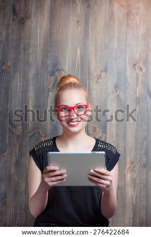 Youth and technology. Young attractive blond woman using tablet computer and looking at camera against wooden wall.