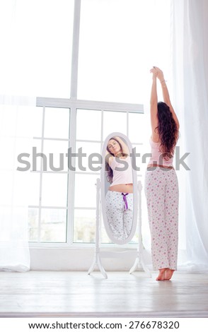 Happy morning. Attractive young woman stretching near mirror at her apartment.