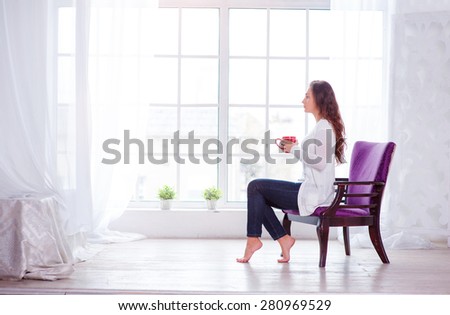 Calm and coziness. Beautiful young woman with cup of tea sitting on armchair at home.