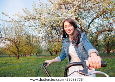 Week end in spring park. Attractive young brunette woman riding on bicycle against nature background.