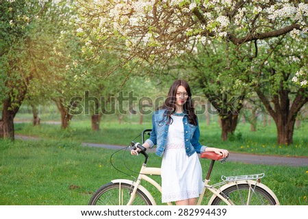 Week end in spring park. Attractive young brunette woman walking with a bicycle against nature background.