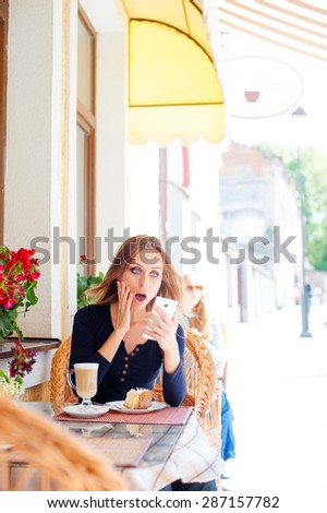 Shocked news. Cafe with wifi. Young amazed woman using smartphone while sitting sidewalk restaurant.