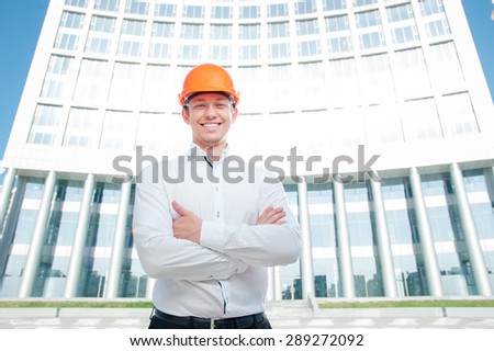 Confident contractor. Cheerful young man in shirt and hardhat keeping arms crossed and smiling while standing outdoors