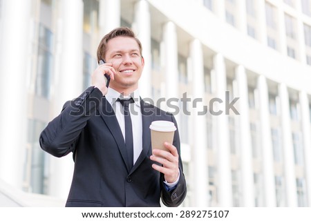 Good talk. Cheerful young business man talking on the mobile phone and holding cup of coffee.
