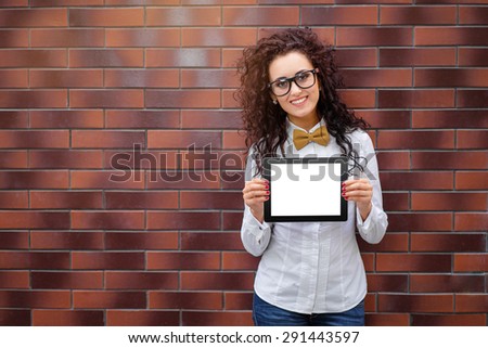 Your text here. Attractive young woman with curl hair showing screen of tablet computer against brick wall.