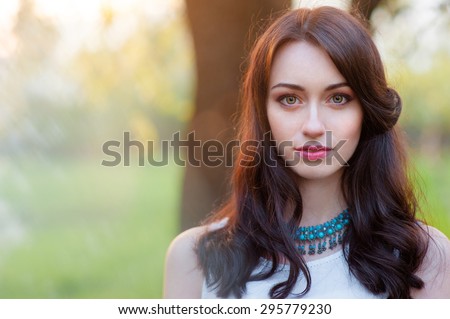 Outdoors portrait of beautiful young brunette woman looking at camera.