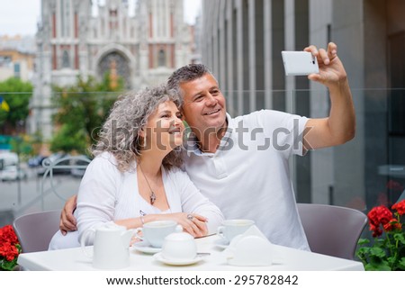 Happy to be together. Attractive elderly family couple taking selfie on smartphone in side walk cafe.