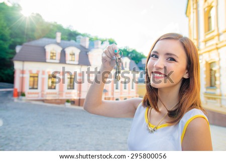 Real estate. Happy broker. Attractive young woman holding keys while standing outdoor against new house.