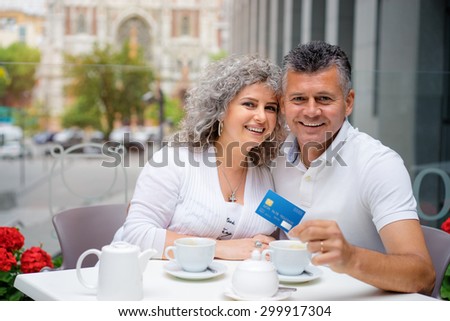 Pay the bill. Attractive elderly family couple holding plastic credit card while siting in sidewalk cafe.