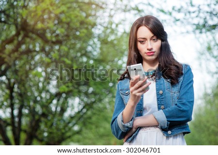 Youth and technology. Amazed young woman using smartphone in green park.