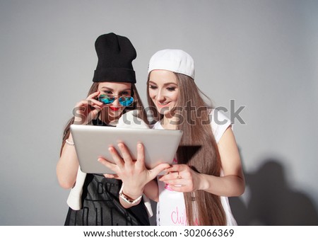 Youth and technology. Attractive twins sisters. Two beautiful smiling young women using tablet computer  together against grey background.