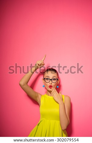 Your text here. Colorful studio portrait of young amazed pretty woman is pointing up.