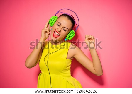 Joy and music. Colorful studio portrait of happy young brunette woman with earphones is dancing and singing.