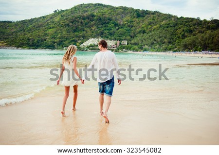 Honeymoon at the sea. Back view of loving couple walking away  at sandy beach