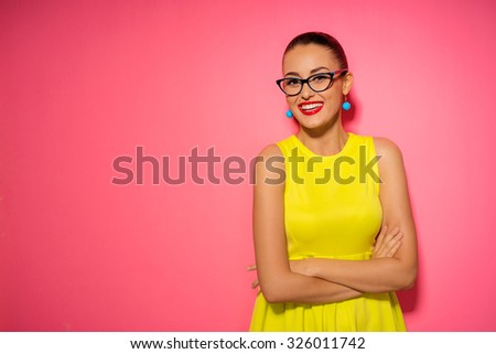 Colorful studio portrait of confident young brunette woman with hands crossed. Pink background.