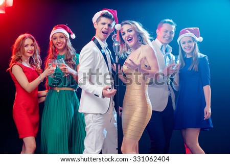 Merry Christmas and Happy New Year! Party and celebration. Group of six happy smiling friends having fun together, singing karaoke in the club.