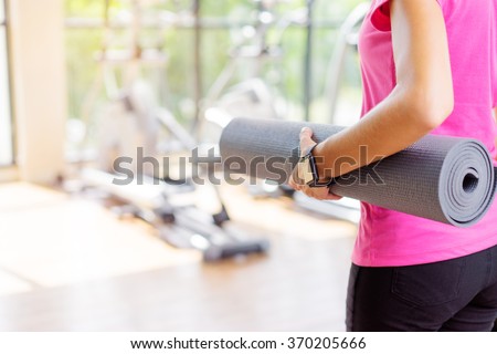 Healthy lifestyle and sport. Close up of young woman holding mat in gym.
